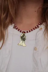 Collar corto de cuentas en tonos rojo y beige, con dije colgante en forma de pez de metal dorado con textura martillada.