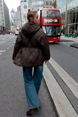Chaqueta acolchada de color marrón oscuro con diseño de costuras onduladas, cuello subido, capucha ajustable con cordones, cierre frontal con cremallera y cintura ajustable con cordones. Cuenta con bolsillos delanteros de vivo y tejido repelente al agua.