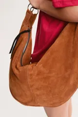Cartera tipo hobo de gran tamaño, confeccionada en cuero descarne color rojo, con diseño artesanal y correa integrada al cuerpo de la cartera.