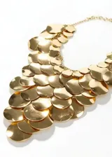 Collar babero dorado compuesto por múltiples capas de lentejuelas o discos metálicos superpuestos que crean un diseño llamativo y texturizado, con cadena ajustable en la parte posterior.
