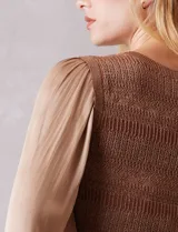 Blusa de punto con torso texturizado en color marrón con hilos de lurex dorados. Presenta un corte peplum con volado en la cintura y mangas largas de satén fluido con volumen, terminadas en puños elásticos fruncidos.