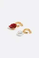 Pendientes de aro dorados con diseño asimétrico, uno con dije de rosa roja en resina y el otro con dije de perla barroca. Cierre de presión.