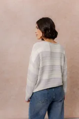 Buzo de tejido liviano con diseño de rayas horizontales en tonos amarillo manteca y blanco, cuello redondo y mangas largas con puños tejidos.