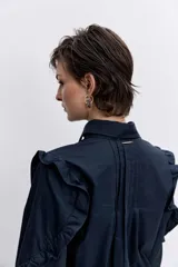 Camisa de color azul oscuro, con cuello clásico, cierre frontal de botones y detalle de volados en los hombros y a lo largo de las mangas largas.