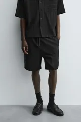 Bermuda de corte relajado color marrón con finas rayas verticales negras. Presenta cintura elástica ajustable con cordón y bolsillos laterales y trasero.