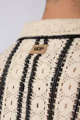 Camisa de manga corta tejida al crochet con diseño de rayas verticales negras sobre una base color crudo. Presenta cuello solapa y cierre frontal con botones.