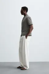 Camisa de punto de manga corta con cuello bowling y cierre frontal de botonadura. Presenta un patrón de rayas horizontales finas en blanco y negro, con ribetes negros en cuello, puños y bajo.