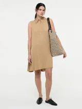 Vestido corto color beige, estilo camisero, sin mangas, con cuello clásico, cierre frontal con botones y bolsillos laterales.