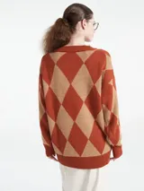 Sweater de punto con escote en V y diseño de rombos en tonos marrón y naranja. Presenta un corte holgado, mangas largas con puños acanalados y terminación de ruedo también acanalada.
