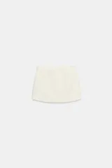 Falda pantalón de tiro bajo color blanco crudo, con diseño de cintura asimétrica y cierre lateral con cremallera oculta en costura.