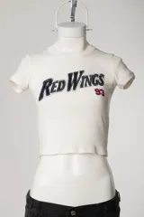 Remera tipo baby tee blanca de manga corta, con cuello redondo y diseño ajustado al cuerpo con estampado y bordado frontal "Red Wings 93".