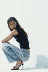 Sandalia de tacón alto fino, color negro, con tiras finas cruzadas en el empeine y un detalle de abalorio rojo y dorado en la unión de las tiras. Posee tira ajustable con hebilla en el tobillo.