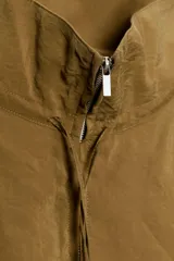 Chaqueta color naranja óxido de tejido fluido, con cuello subido, manga larga acabada en elástico, bolsillos laterales de vivo, bajo elástico y cierre frontal con cremallera.