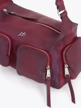 Cartera de hombro confeccionada en cuero vacuno color bordó con acabado desgastado. Presenta múltiples bolsillos exteriores con cierre en el frente, dorso y laterales, herrajes metálicos plateados y logo de la marca aplicado en el frente.