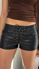 Short negro de tiro bajo confeccionado en cuero sintético, con cordones cruzados ajustables al frente y detalles de tachas metálicas en los bolsillos.