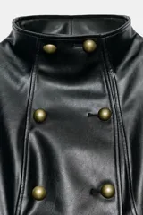 Chaqueta entallada de efecto piel en color negro, con cuello subido y cierre frontal cruzado con botones metálicos dorados. Cuenta con manga larga con trabillas en los puños y hombreras decorativas.