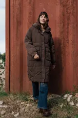 Campera larga acolchonada color marrón, con diseño midi, capucha amplia, cierre frontal con cremallera y broches, y bolsillos delanteros con tapa.