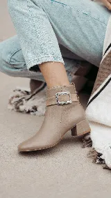 Bota corta de cuero color chocolate, con diseño minimalista, taco cuadrado de 4 cm y una hebilla metálica decorativa en el tobillo sobre una banda de gamuza.