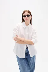 Camisa de algodón blanca, de corte clásico con cuello camisero, cierre frontal con botones, mangas largas con puños y bolsillo frontal en el pecho.