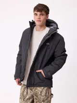 Campera técnica de invierno marca Rusty, color negro, con capucha ajustable, cierre frontal con solapa y bolsillos laterales. Presenta logo de la marca estampado en blanco en la manga y en el pecho.
