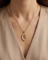 Collar de bronce dorado con cadena fina y dije ovalado con la figura de una virgen incrustada con pequeños cristales y una perla central.