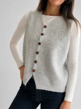 Chaleco tejido de punto en color gris melange, con escote en V y cierre frontal mediante una hilera de botones marrones. Presenta un diseño clásico con terminaciones acanaladas en el ruedo.