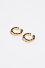 Aros tipo argolla metálicos en tono dorado con esmalte negro y letras grabadas en relieve con el nombre de la marca.