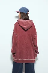 Buzo con capucha de calce relajado, confeccionado en tela con efecto lavado desgastado. Presenta costuras a la vista en color contrastante y un bolsillo frontal tipo canguro.