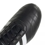 Championes Adidas modelo Taekwondo Lace, de diseño minimalista en color negro con las tres tiras características en blanco y detalle en el talón. Presentan una silueta de perfil bajo con costuras reforzadas en la puntera y suela de goma color caramelo.