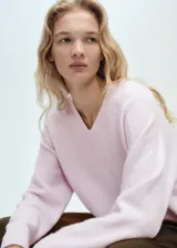 Jersey de punto color rosado con cuello en V, manga larga y diseño recto con terminaciones acanaladas.