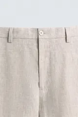 Pantalón de traje regular fit confeccionado en tejido de lino, con bolsillos laterales y bolsillos traseros de vivo con botón. Presenta cierre frontal con cremallera y botón.