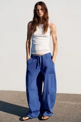 Pantalón cargo de tiro medio con corte oversize, bolsillos laterales con solapa en las piernas y bolsillos de plastrón en el delantero. Cuenta con trabillas, lazadas ajustables en la cintura y cierre frontal con cremallera y botón.