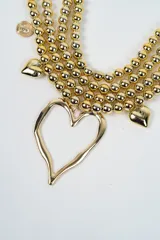 Collar multicapa compuesto por tres hileras de esferas metálicas plateadas. Presenta un dije central grande en forma de corazón irregular, acompañado por dijes más pequeños de corazones y monedas grabadas distribuidos a lo largo de las cadenas.
