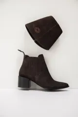 Bota de cuero color chocolate con diseño versátil que incluye una polaina desmontable. Presenta punta fina, taco cuadrado y un detalle bordado en la parte superior de la caña.
