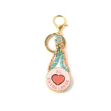 Llavero con dije circular metálico color dorado, esmaltado en rosa con un corazón central y la inscripción 'EXTRA LARGE'. Incluye una argolla y un gancho mosquetón dorados, unidos por cordones trenzados en tonos naranja, turquesa y amarillo.