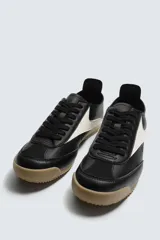 Zapatilla de cordones estilo retro, color negro con detalles en blanco y suela de goma color caramelo.