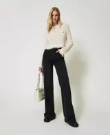 Sweater de punto calado color crema, con cuello redondo, manga larga, flecos en el ruedo y dos bolsillos de parche con botones metálicos con el logo de la marca.