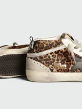Zapatillas Golden Goose modelo Mid Star con diseño de caña media, confeccionadas en piel con estampado de leopardo y detalles en gamuza beige. Presentan una estrella lateral en color negro, cordones en tono neutro y suela con efecto desgastado.