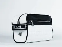 Necessaire Tiffosi de diseño rectangular, combinando paneles en blanco y negro. Presenta una textura acolchada tipo cuadrillé en la parte inferior, cierre metálico frontal y una banda lateral con el logo de la marca. Incluye un aplique metálico circular con el logo en el lateral.