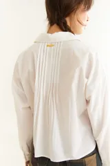 Camisa de corte boxy y calce holgado, color bordó, con cuello clásico, cierre frontal de botones y detalle de tablas con recortes diagonales en el pecho.