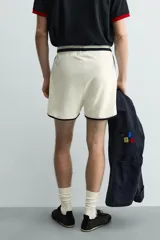 Short deportivo de tejido de punto con estructura abierta, color blanco con vivos a contraste en azul marino. Presenta cintura elástica, bolsillos frontales, aberturas laterales en el bajo y etiquetas conmemorativas de la Copa Mundial de la FIFA Francia 98.