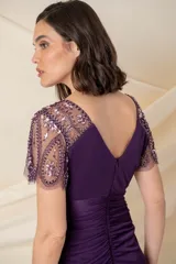 Vestido largo de fiesta color violeta, con cuerpo de jersey y falda de gasa con diseño drapeado y sobrecapa. Presenta escote en V y mangas cortas de tul bordado con pedrería al tono.