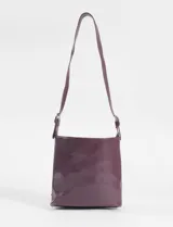 Cartera bandolera de cuero vegano color bordó, con diseño estructurado y detalle de cuatro hebillas metálicas decorativas en el lateral. Cuenta con correa larga ajustable y cierre principal.
