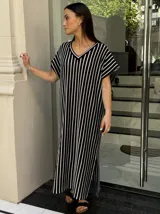 Vestido largo de tejido de punto con diseño de rayas verticales en blanco y negro. Presenta escote en V, mangas cortas y tajos laterales en el ruedo para mayor movimiento.