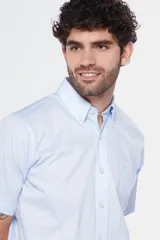 Camisa de manga corta color celeste claro, con cuello abotonado (button-down) y un bolsillo de parche en el pecho.