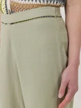 Pantalón de corte recto y tiro alto, confeccionado en una mezcla de lino orgánico y viscosa. Presenta detalles de calado decorativo en la cintura y en el ruedo de las piernas.
