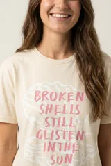 Remera de manga corta color beige, confeccionada en 100% algodón, con cuello redondo y estampa frontal con texto en tonos rosados.