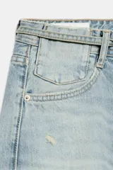 Jeans de tiro medio y corte baggy con cinco bolsillos, trabillas y rotos decorativos. Cuenta con detalle de cinturón confeccionado en el mismo tejido y cierre frontal con cremallera y botón metálico.