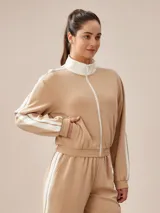 Campera deportiva tostada con cierre frontal blanco, cuello alto y bandas blancas en las mangas.