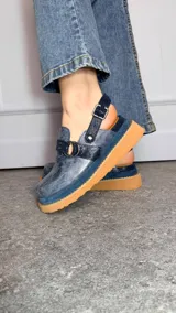 Zuecos cerrados tipo sandalias de plataforma, confeccionados en cuero con efecto craquelado en tono azul, con tiras texturizadas, argollas metálicas decorativas y tira trasera con hebilla regulable.